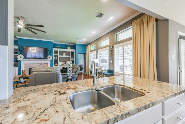 kitchen with sink, ceiling fan, light stone countertops, a fireplace, and ornamental molding