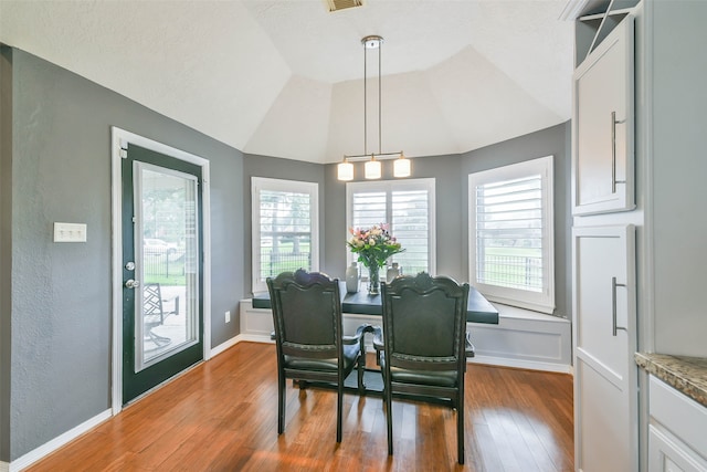 dining area with wood-type flooring, an inviting chandelier, and lofted ceiling