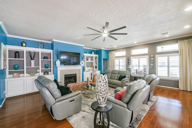 living room featuring ornamental molding, a textured ceiling, ceiling fan, a tile fireplace, and hardwood / wood-style flooring