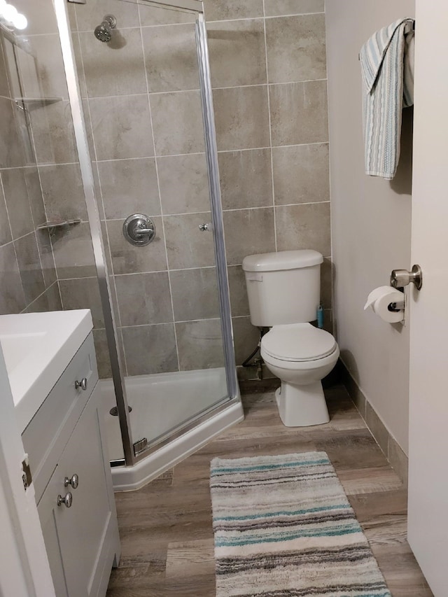 bathroom with tile walls, toilet, a shower with shower door, wood-type flooring, and vanity