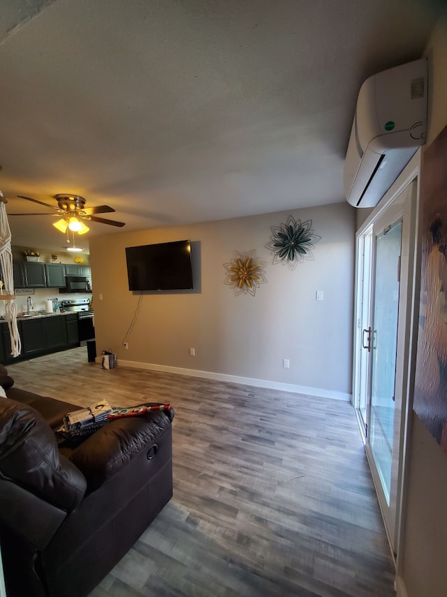 living room featuring wood-type flooring, ceiling fan, and an AC wall unit