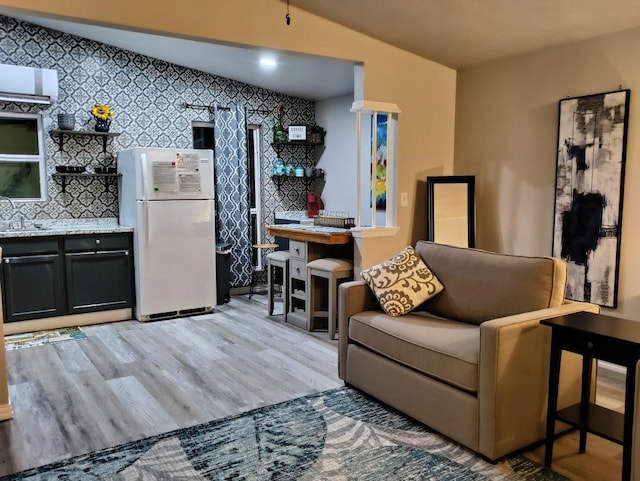 living room with light hardwood / wood-style floors, sink, and vaulted ceiling