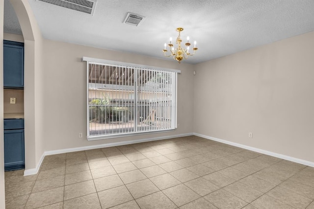 empty room featuring a notable chandelier, a textured ceiling, and light tile flooring