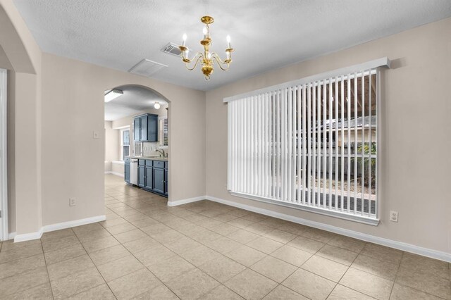 tiled spare room with a wealth of natural light, sink, a chandelier, and a textured ceiling