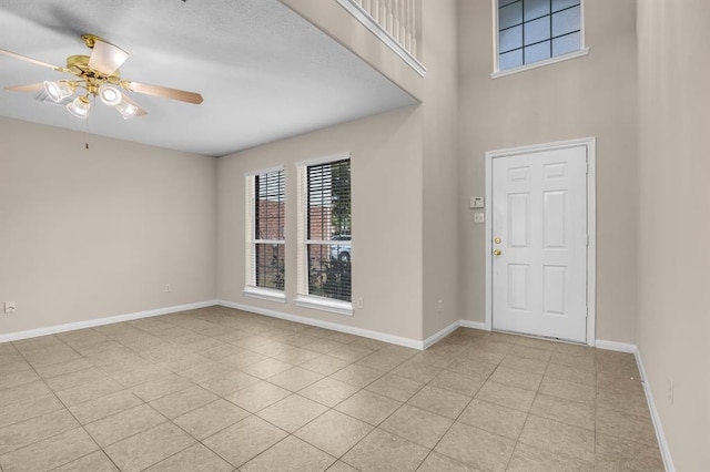 foyer entrance with a towering ceiling, ceiling fan, and light tile floors