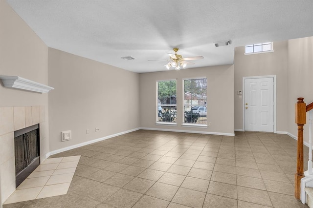 unfurnished living room with ceiling fan, a textured ceiling, a tile fireplace, and light tile floors