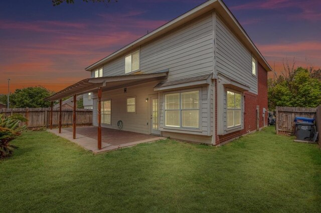 back house at dusk featuring a lawn and a patio area