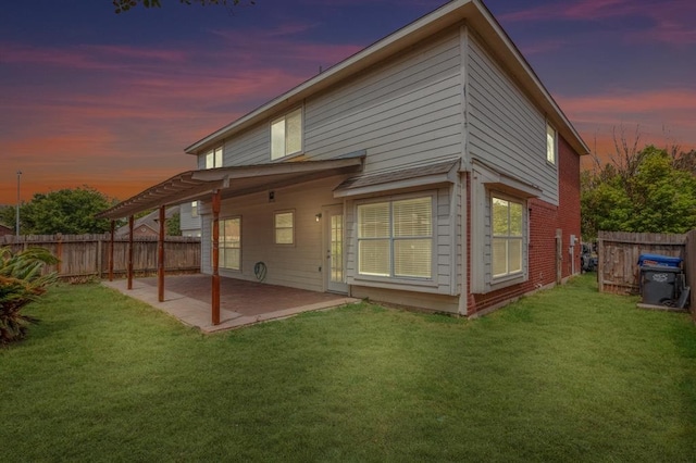 back house at dusk featuring a yard and a patio