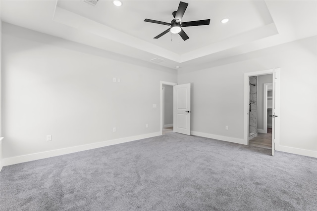 unfurnished bedroom with a tray ceiling, ceiling fan, carpet, and a spacious closet