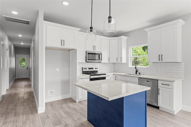 kitchen featuring stainless steel appliances, sink, pendant lighting, a center island, and white cabinetry