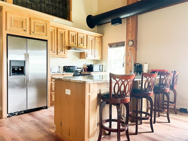 kitchen with light stone countertops, light brown cabinetry, light wood-type flooring, black appliances, and a breakfast bar area