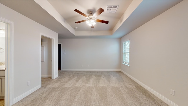 unfurnished room with light colored carpet, a raised ceiling, and ceiling fan