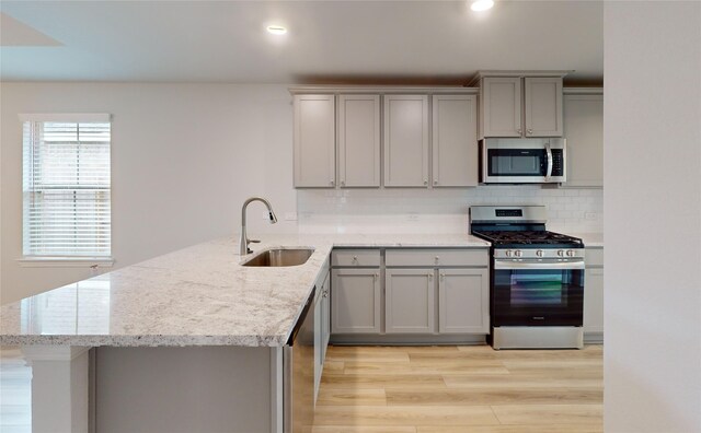 kitchen with light hardwood / wood-style flooring, stainless steel appliances, sink, kitchen peninsula, and backsplash