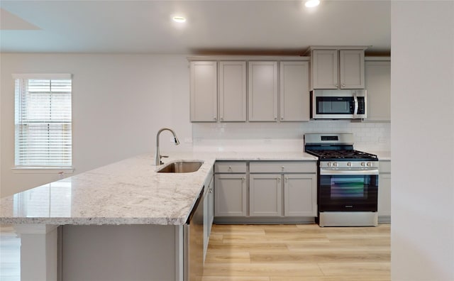 kitchen with appliances with stainless steel finishes, sink, gray cabinetry, light stone counters, and kitchen peninsula