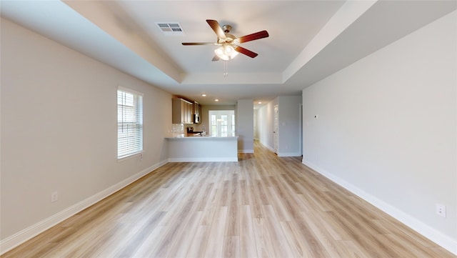 unfurnished living room featuring ceiling fan, a raised ceiling, and light hardwood / wood-style floors