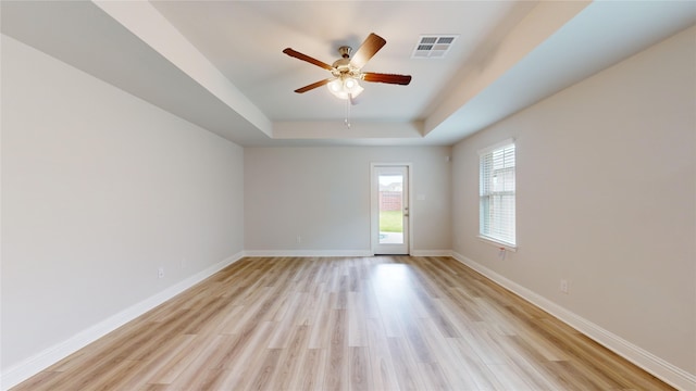 spare room with light hardwood / wood-style floors, a raised ceiling, and ceiling fan