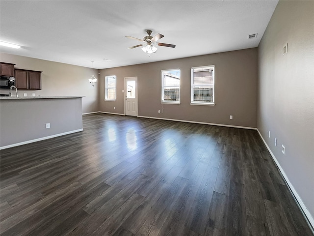 unfurnished living room featuring sink, ceiling fan with notable chandelier, and dark wood-type flooring