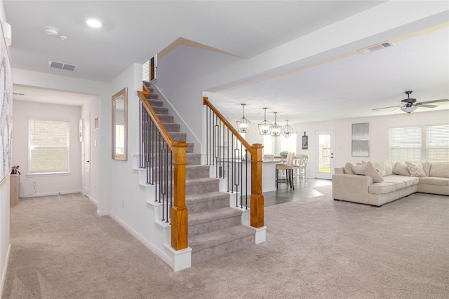 staircase featuring ceiling fan with notable chandelier and carpet