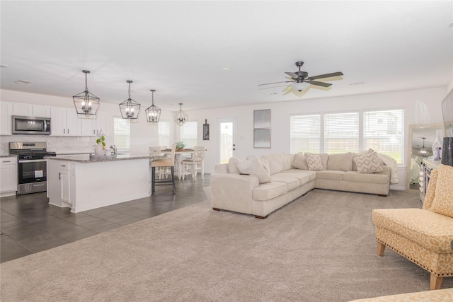 living room featuring dark colored carpet and ceiling fan with notable chandelier