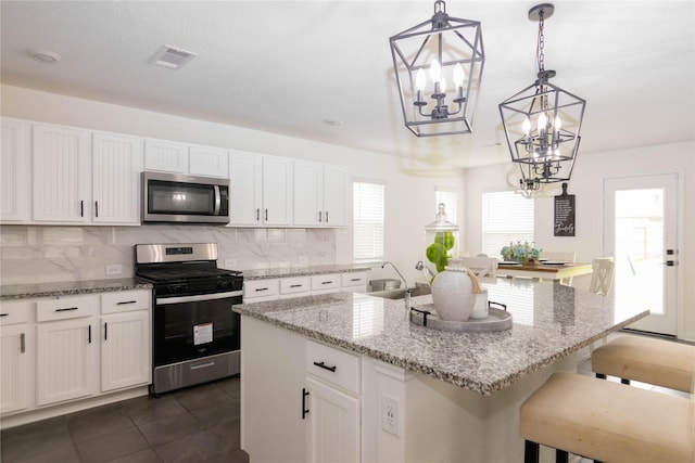 kitchen with a breakfast bar, hanging light fixtures, a center island with sink, stainless steel appliances, and white cabinets