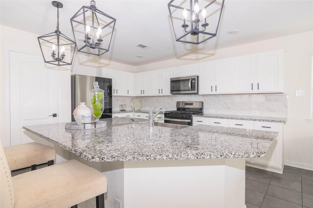 kitchen with white cabinetry, decorative light fixtures, stainless steel appliances, and a center island with sink