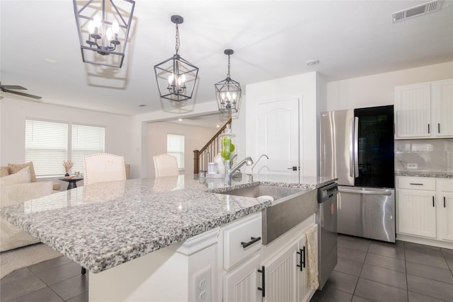 kitchen with white cabinets, decorative backsplash, hanging light fixtures, stainless steel appliances, and a center island with sink