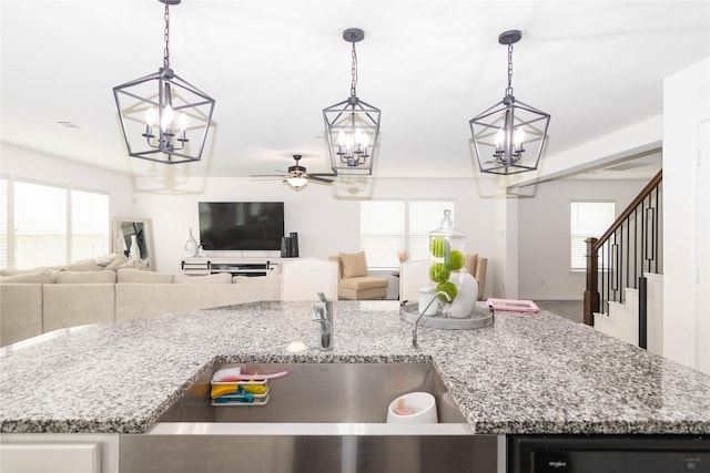 kitchen with pendant lighting, sink, ceiling fan with notable chandelier, and light stone countertops