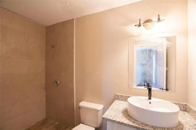 bathroom featuring tiled shower, a textured ceiling, large vanity, and toilet