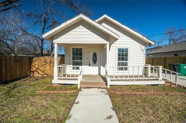 bungalow-style home with covered porch, fence, and a front lawn