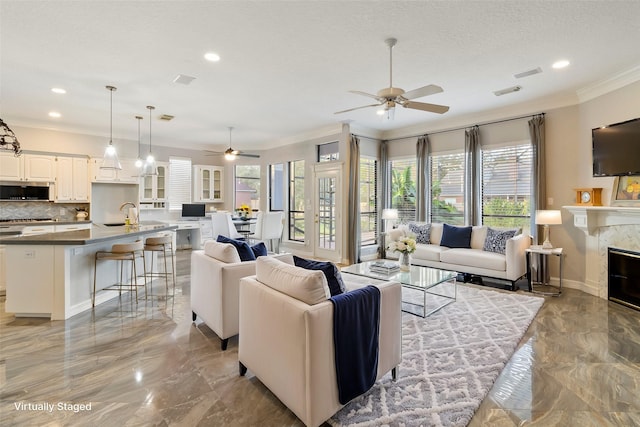 living room featuring ceiling fan, sink, crown molding, and a high end fireplace