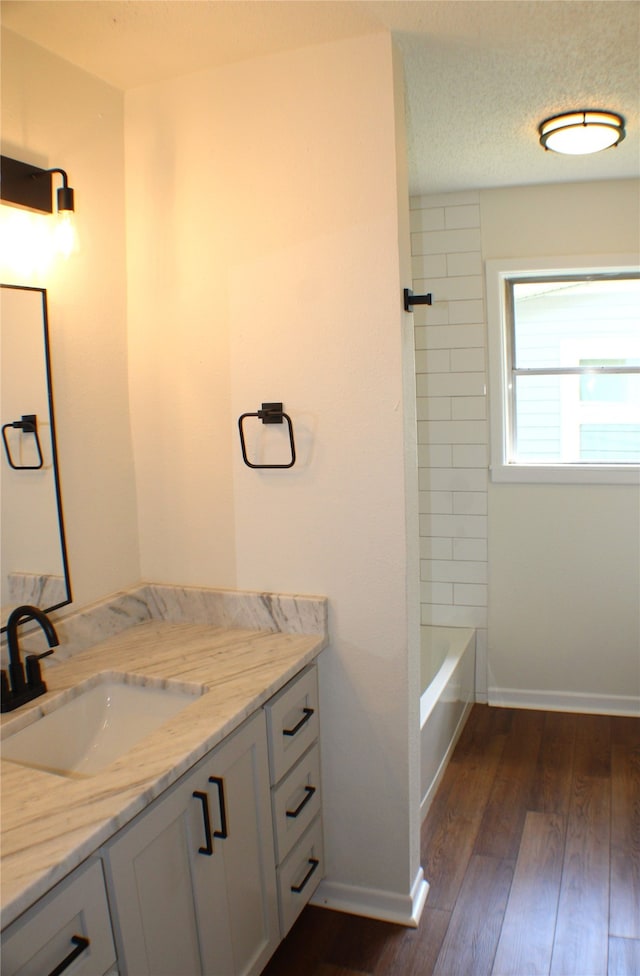 bathroom with tiled shower / bath combo, a textured ceiling, hardwood / wood-style flooring, and vanity