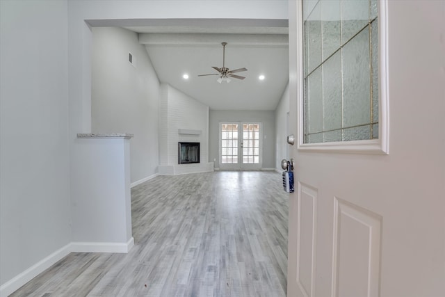 unfurnished living room featuring french doors, a brick fireplace, ceiling fan, beamed ceiling, and light hardwood / wood-style flooring