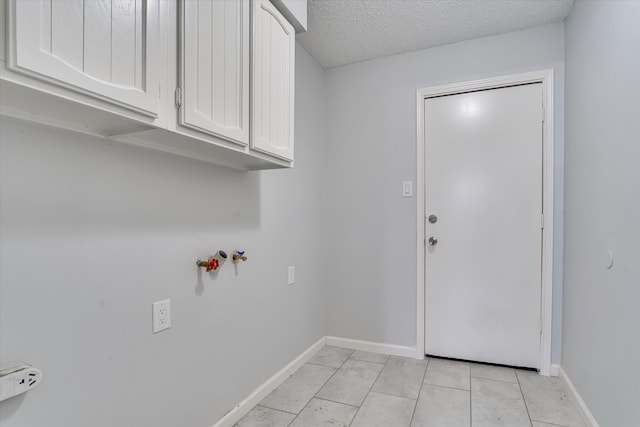 laundry area with cabinets, a textured ceiling, and light tile patterned floors