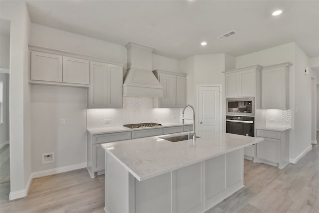 kitchen with tasteful backsplash, a kitchen island with sink, sink, light hardwood / wood-style flooring, and stainless steel appliances