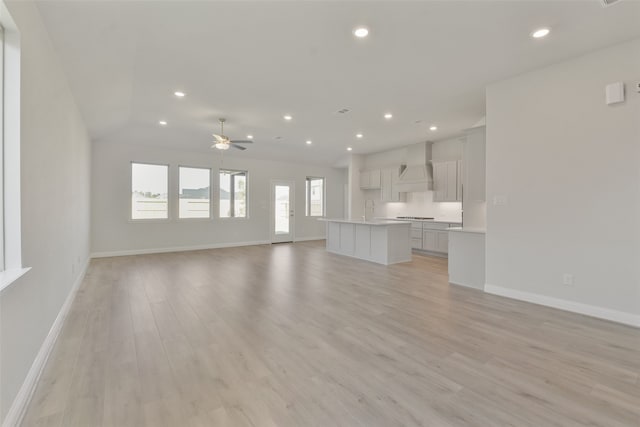 unfurnished living room featuring vaulted ceiling, light hardwood / wood-style floors, ceiling fan, and sink