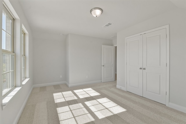 unfurnished bedroom featuring multiple windows, light colored carpet, and a closet