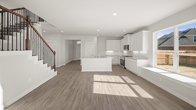 kitchen featuring light wood-type flooring, stainless steel appliances, sink, white cabinets, and an island with sink