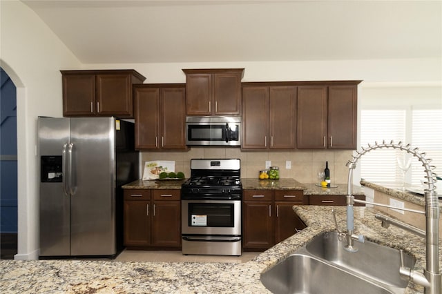 kitchen featuring sink, light stone counters, tasteful backsplash, dark brown cabinets, and appliances with stainless steel finishes