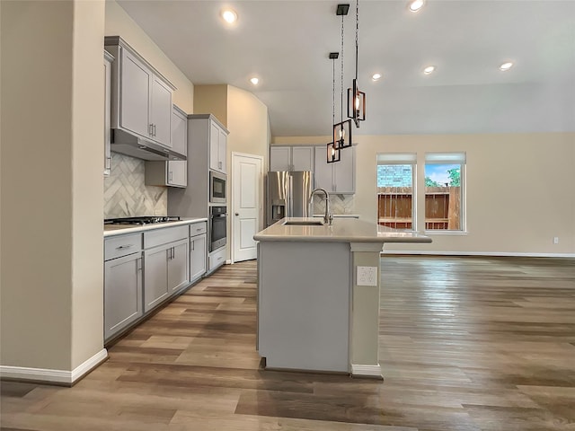 kitchen with appliances with stainless steel finishes, gray cabinets, a kitchen island with sink, and pendant lighting