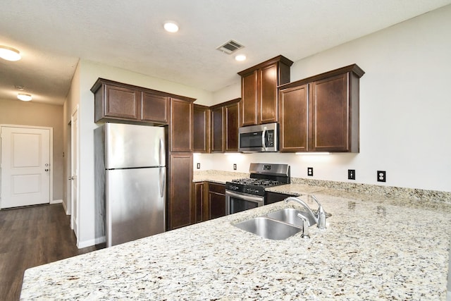 kitchen with stainless steel appliances, dark hardwood / wood-style floors, light stone countertops, dark brown cabinetry, and sink