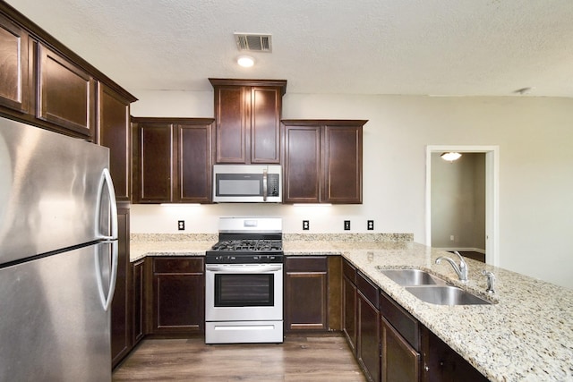 kitchen with light stone countertops, stainless steel appliances, sink, dark hardwood / wood-style floors, and kitchen peninsula