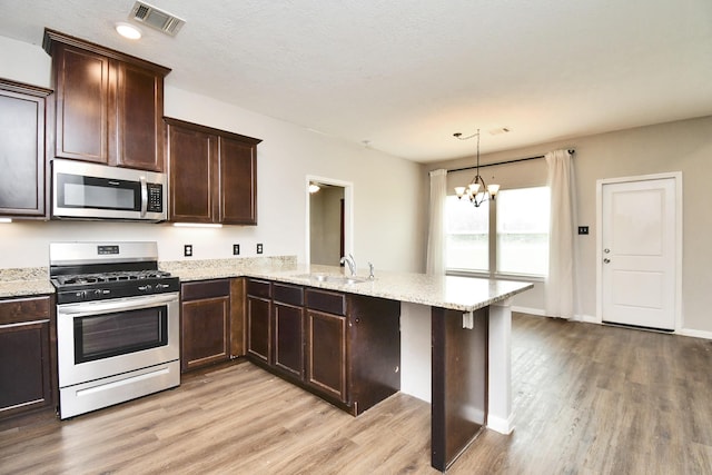 kitchen featuring kitchen peninsula, stainless steel appliances, hanging light fixtures, a chandelier, and sink