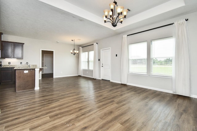 unfurnished living room with dark wood-type flooring, sink, a raised ceiling, and a notable chandelier