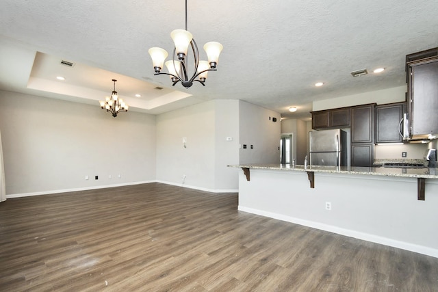 kitchen featuring a raised ceiling, a kitchen bar, stainless steel fridge, and hanging light fixtures