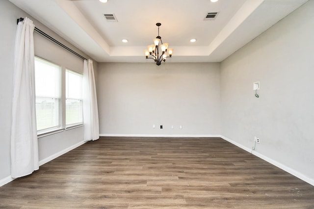 spare room featuring a tray ceiling, dark hardwood / wood-style floors, and a chandelier