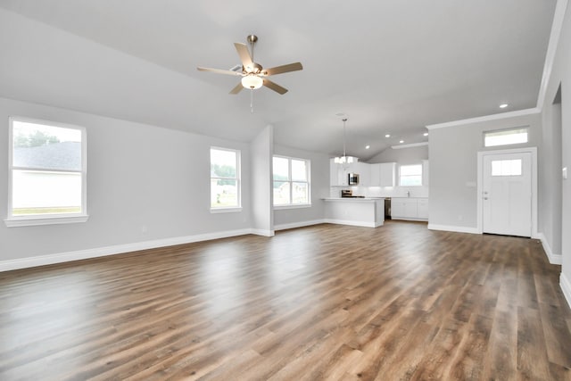 unfurnished living room with ceiling fan with notable chandelier, dark hardwood / wood-style flooring, crown molding, and vaulted ceiling