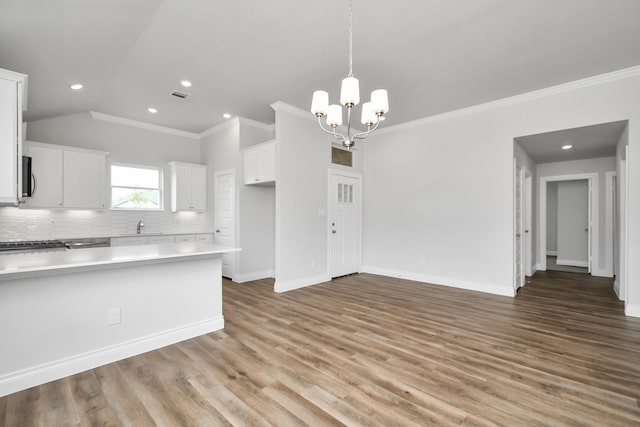 kitchen with backsplash, crown molding, a notable chandelier, white cabinetry, and wood-type flooring