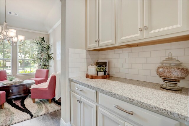 kitchen with white cabinetry, light stone countertops, hanging light fixtures, tasteful backsplash, and ornamental molding