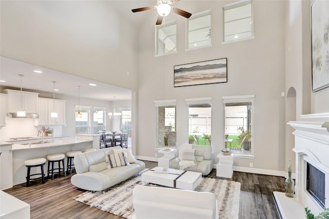 living room with dark wood-style floors, a fireplace with raised hearth, ceiling fan, and baseboards