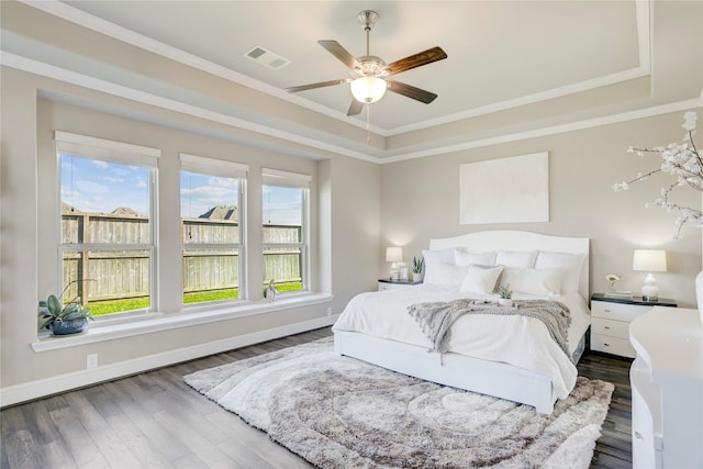 bedroom featuring a tray ceiling, crown molding, ceiling fan, and dark wood-type flooring